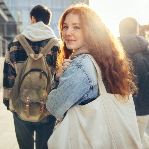 Female student glancing back while going for a class in college. Girl walking with friends going for class in high school.